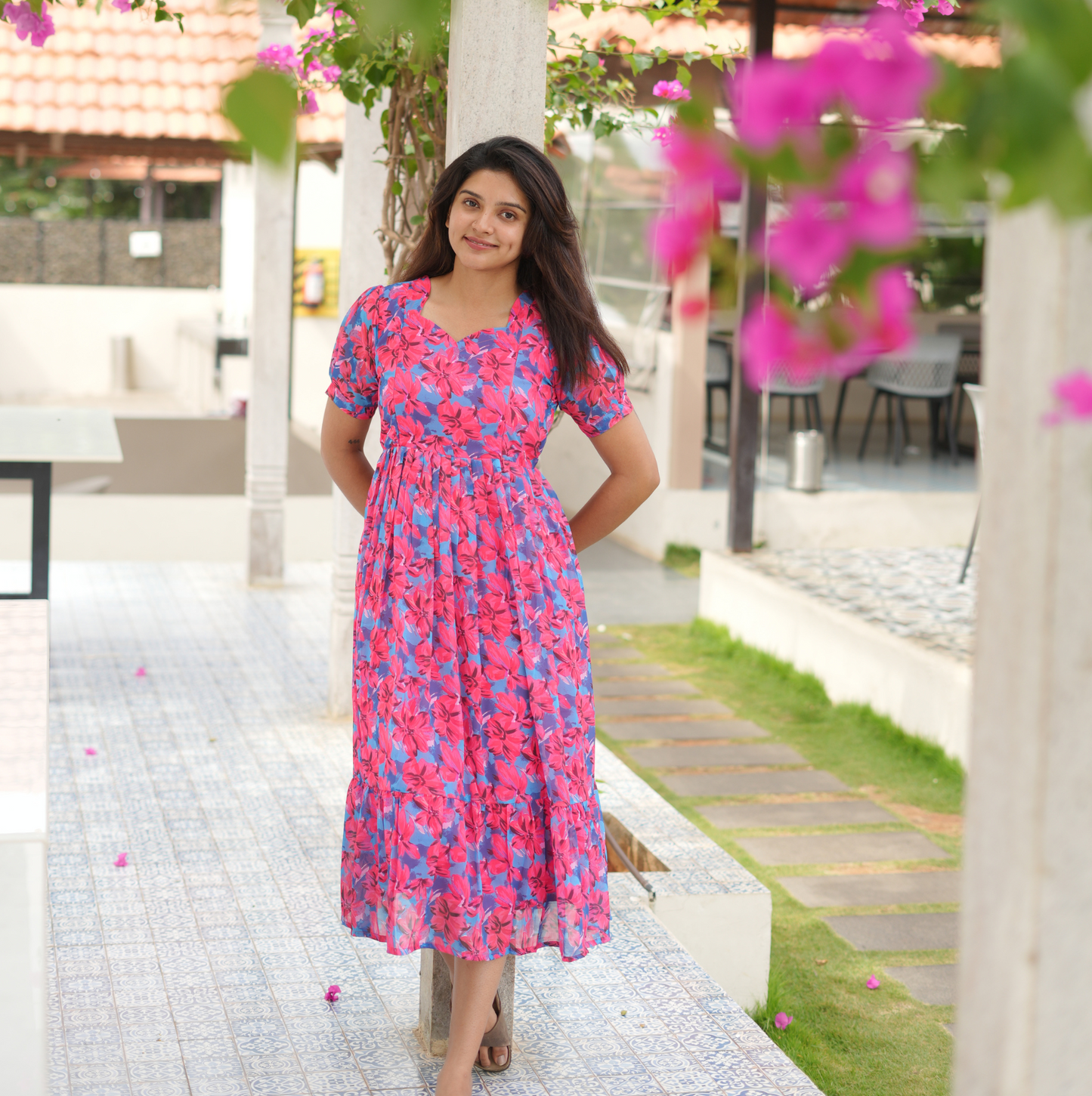 Woman in a pink floral dress standing outdoors with pink flowers in the foreground