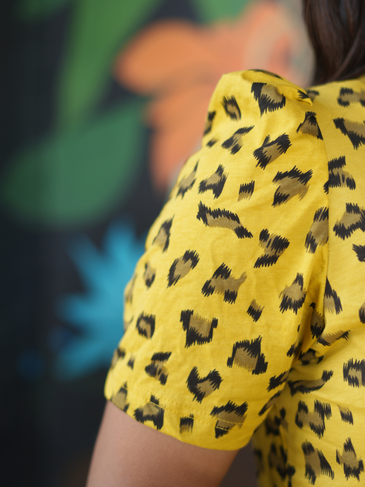 Yellow fabric with black pattern, possibly a shirt or dress, against a blurred background.