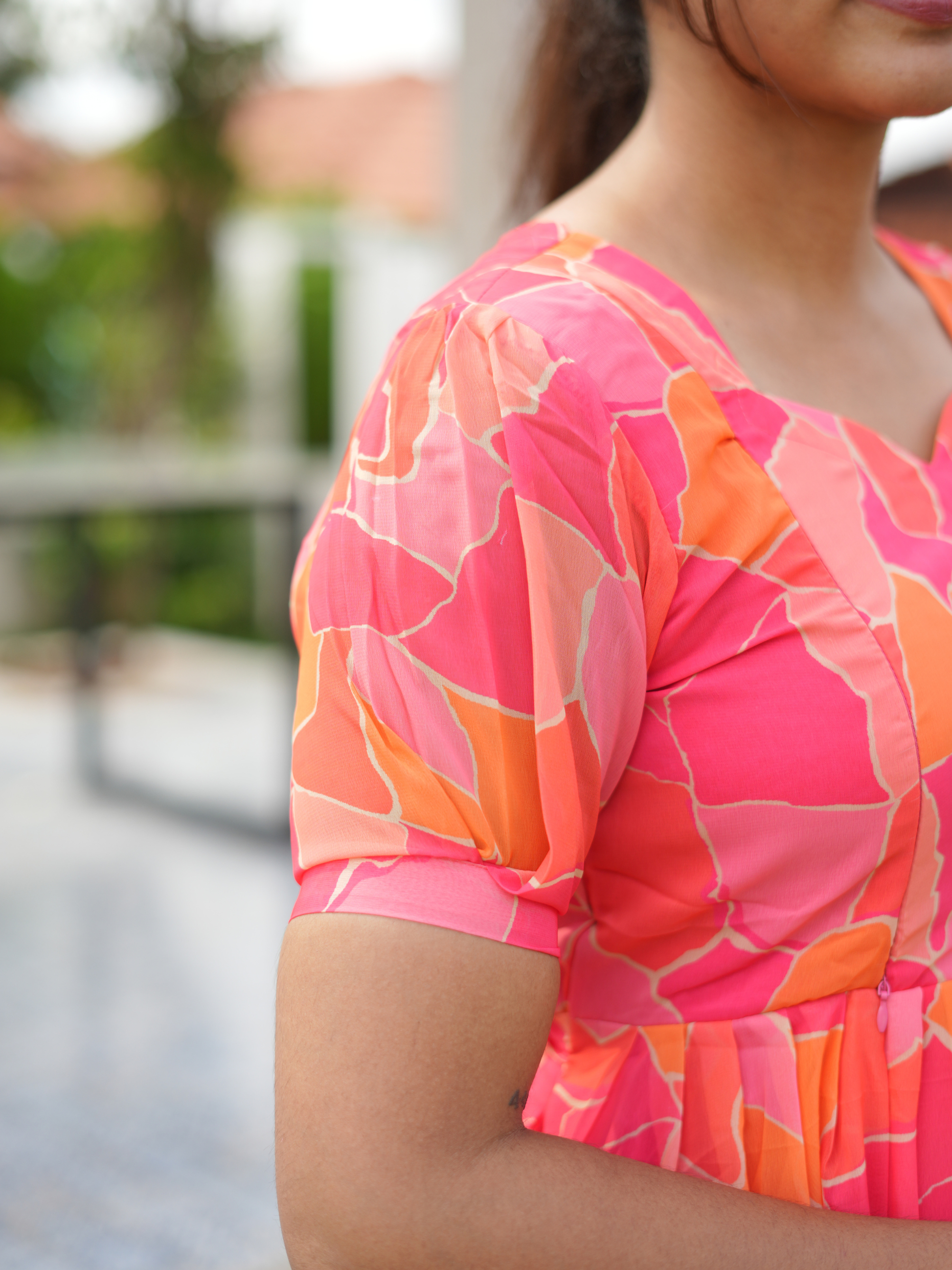 Close-up of a woman wearing a vibrant pink and orange patterned top outdoors.