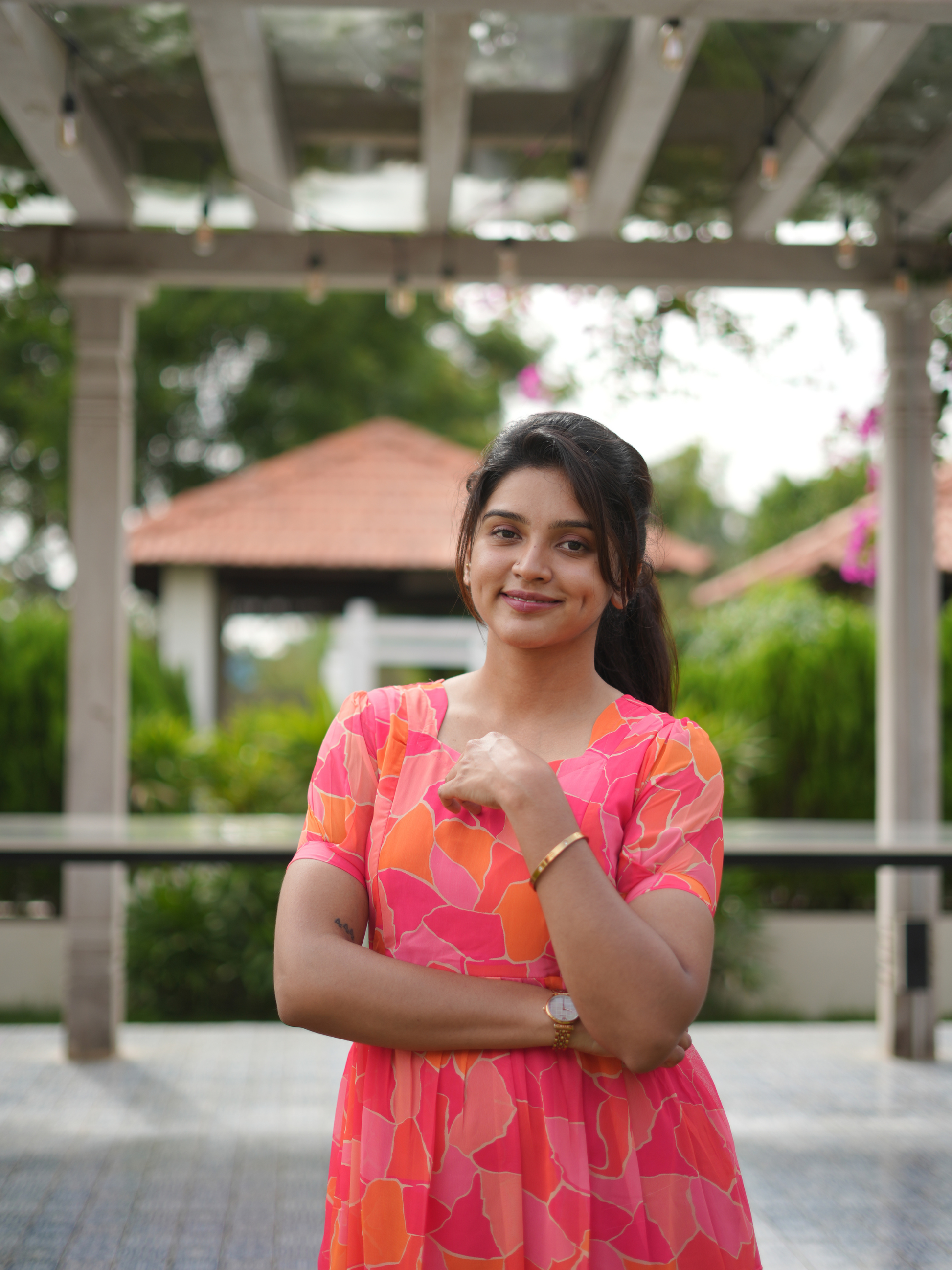 Woman in a pink and orange dress standing outdoors with greenery in the background