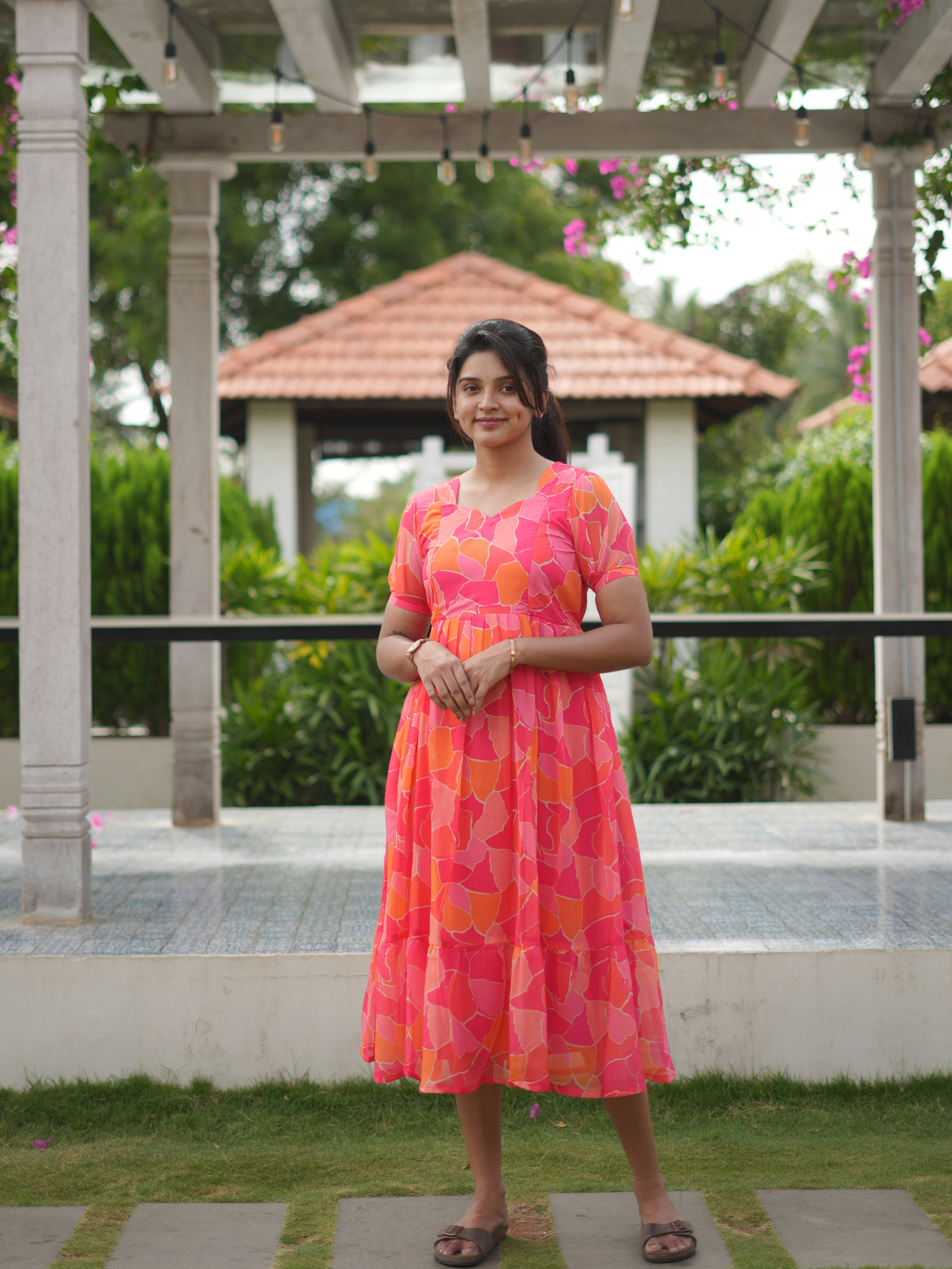 Woman in a colorful dress standing in a garden setting with a gazebo in the background.