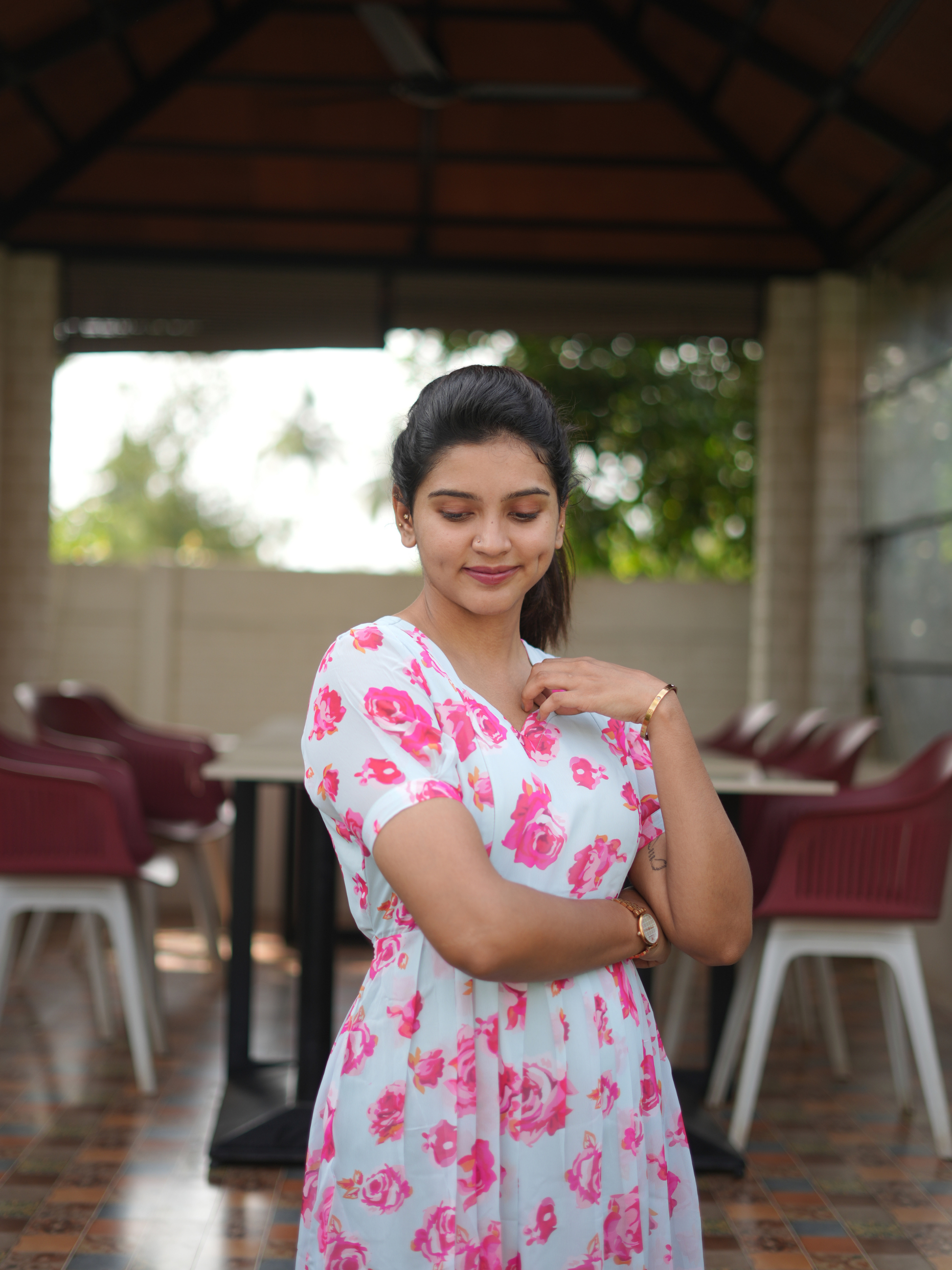Woman in a light blue dress with pink floral pattern standing in an outdoor setting.