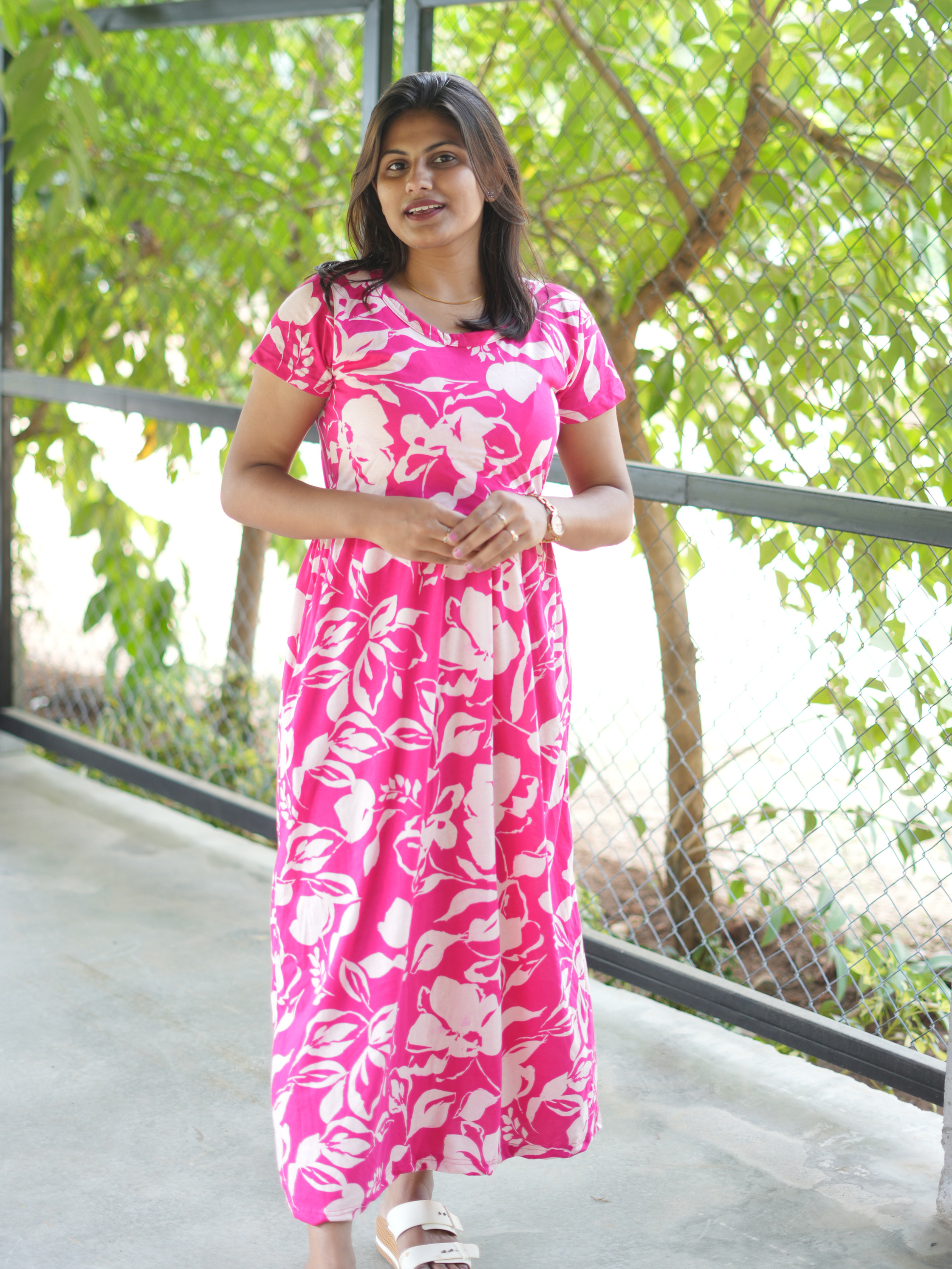 Woman wearing a pink floral dress standing outdoors with greenery in the background