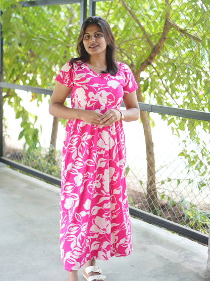 Woman wearing a pink floral dress standing outdoors with greenery in the background