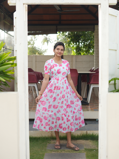 Woman wearing a pink floral dress standing outdoors near a white structure.