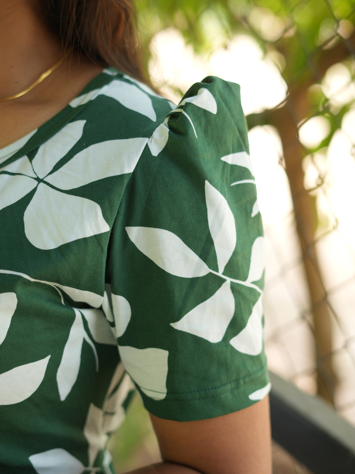 A green and white leaf-patterned shirt worn by a woman with a blurred natural background