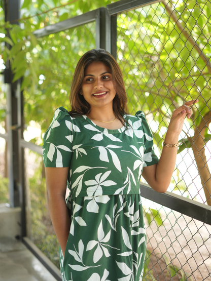 Woman wearing a green dress with white floral pattern standing outdoors.