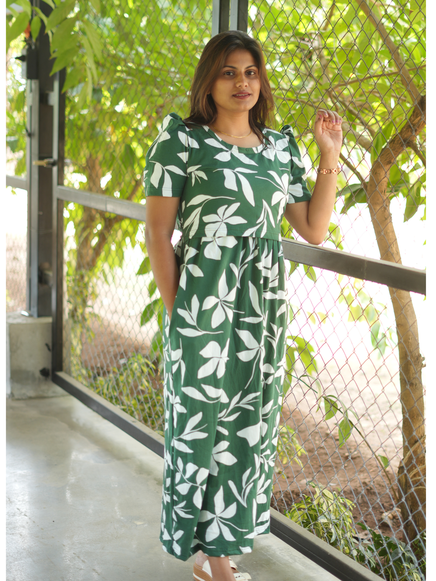 Woman wearing a green dress with white floral pattern standing outdoors.