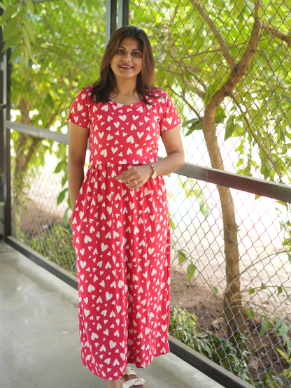 Woman wearing a red dress with white patterns standing outdoors with greenery in the background