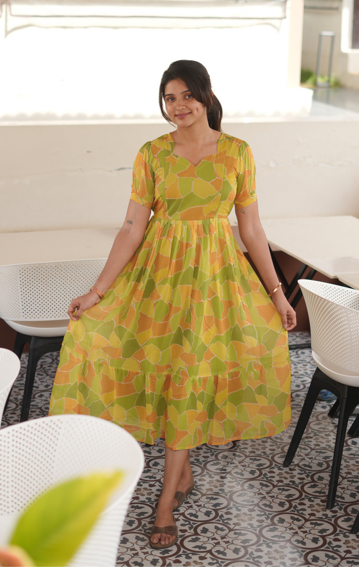 Woman wearing a yellow and green patterned dress in an indoor setting.