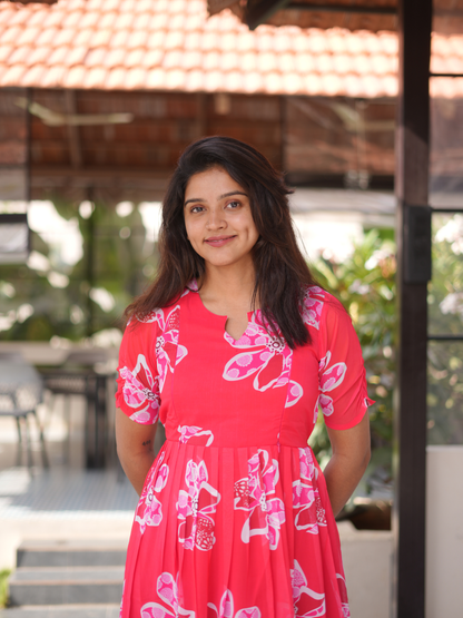 Woman wearing a pink dress with white floral patterns outdoors.