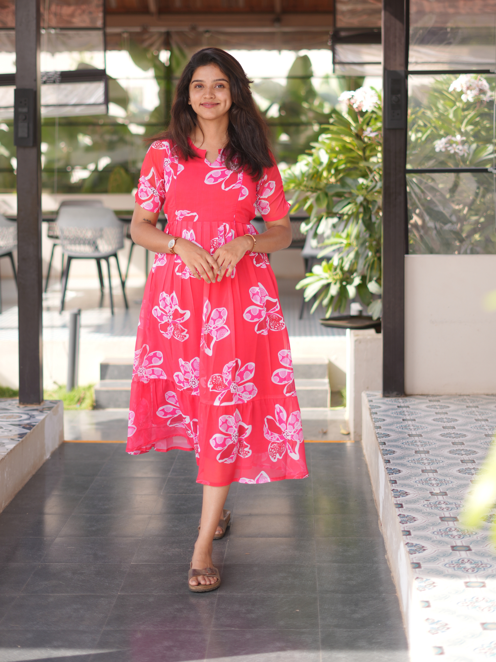 Woman in a pink floral dress standing outdoors with greenery in the background