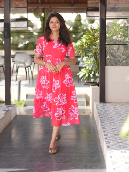 Woman in a pink floral dress standing outdoors with greenery in the background