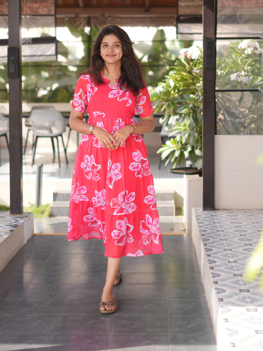 Woman in a pink floral dress standing outdoors with greenery in the background
