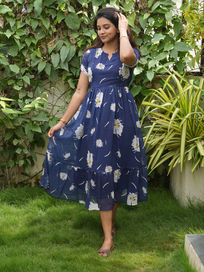 A woman wearing a blue floral dress standing in a garden.