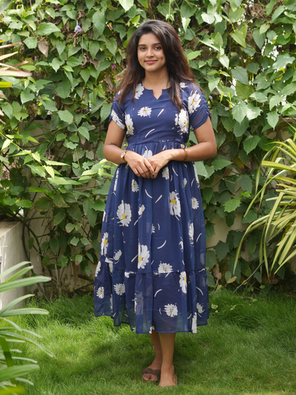 Woman wearing a blue floral dress standing in front of green foliage