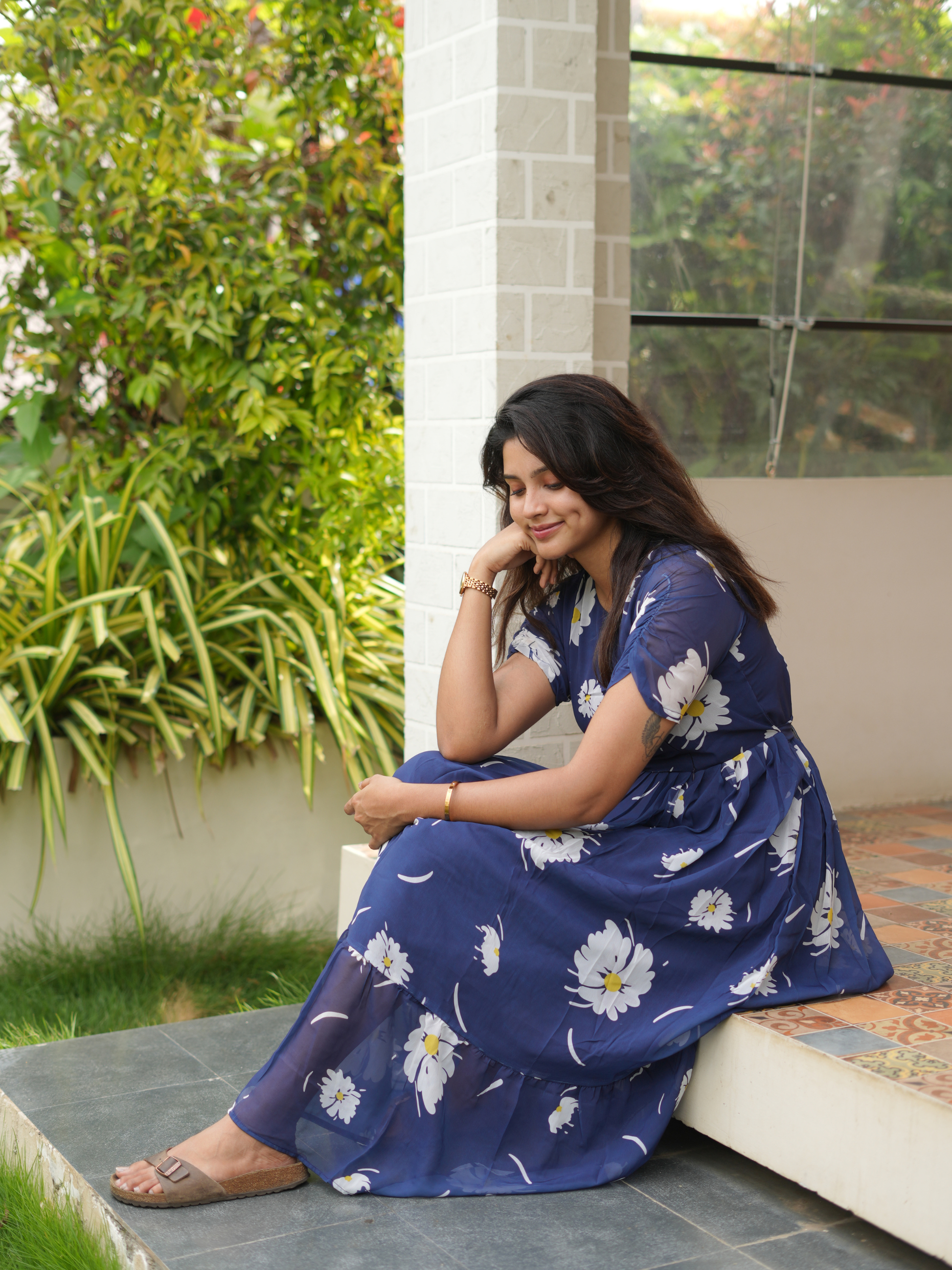 Woman in a blue floral dress sitting outdoors on a stone ledge.