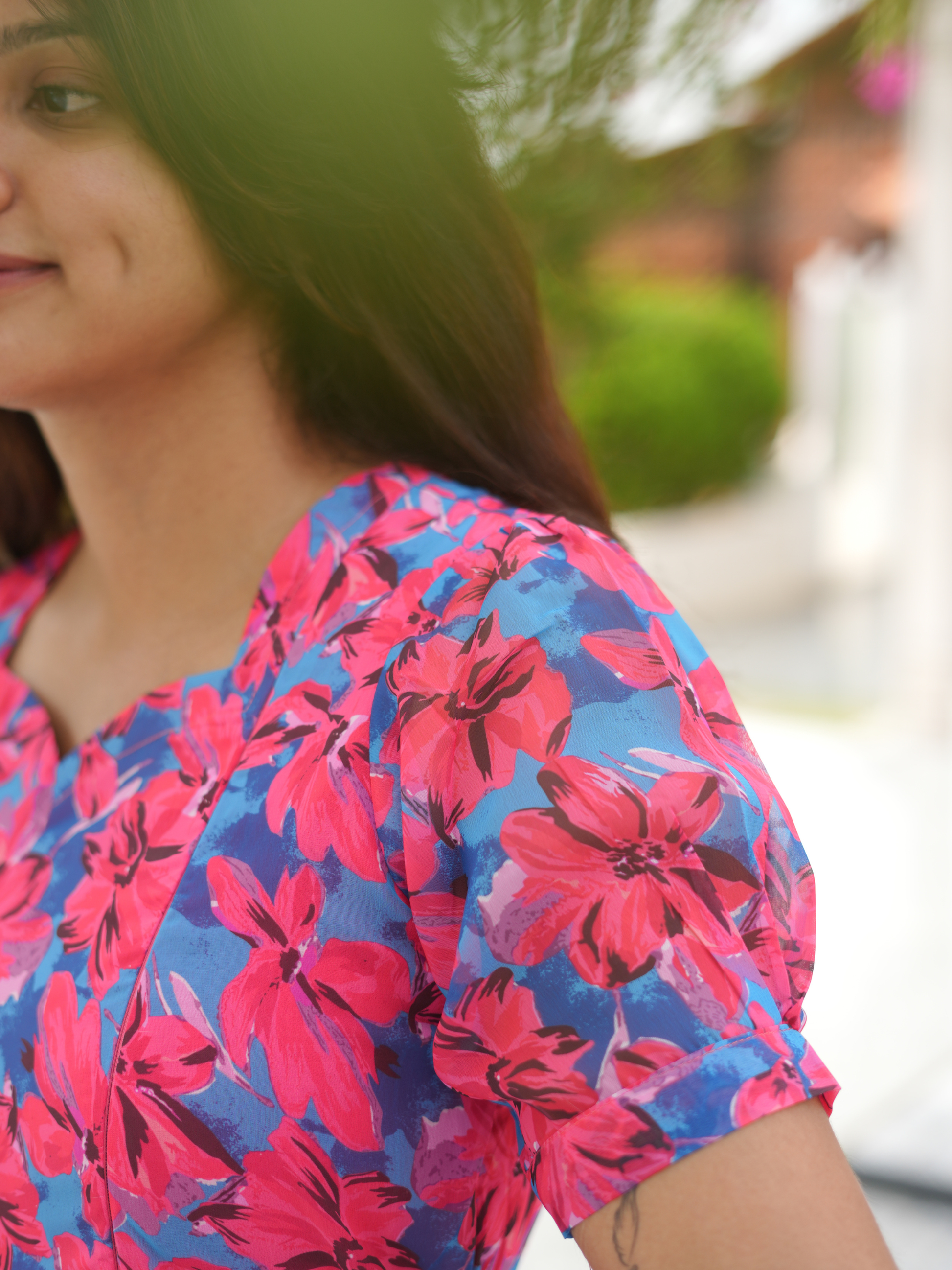Person wearing a colorful floral dress with a blurred outdoor background