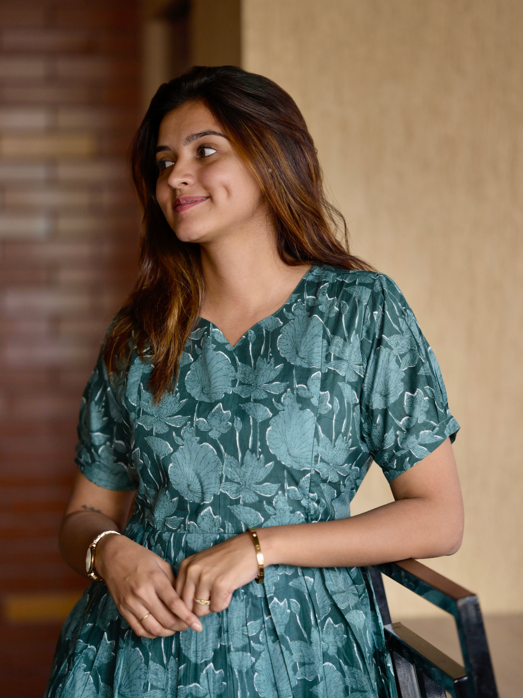 A woman wearing a green floral maxi dress with a V-neckline, featuring visible zippers and a pocket on the right side.