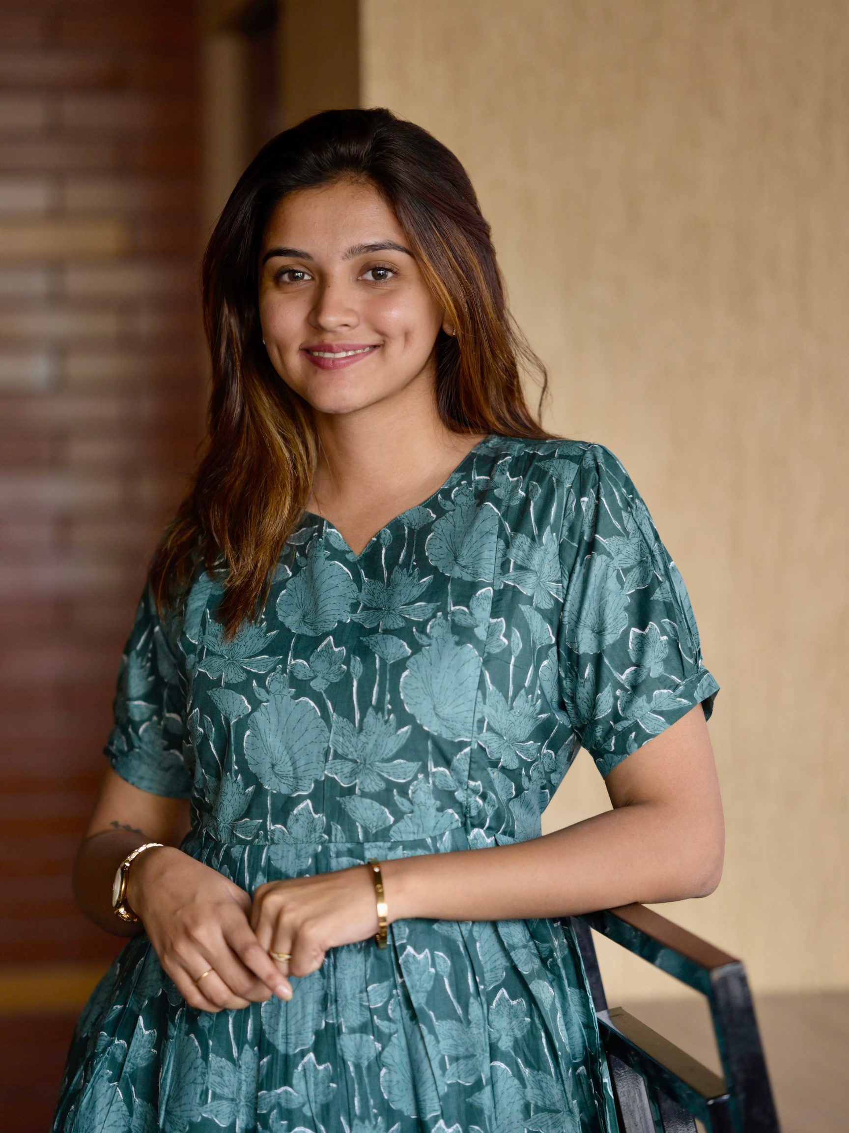 A woman wearing a green floral maxi dress with a V-neckline, featuring visible zippers and a pocket on the right side.