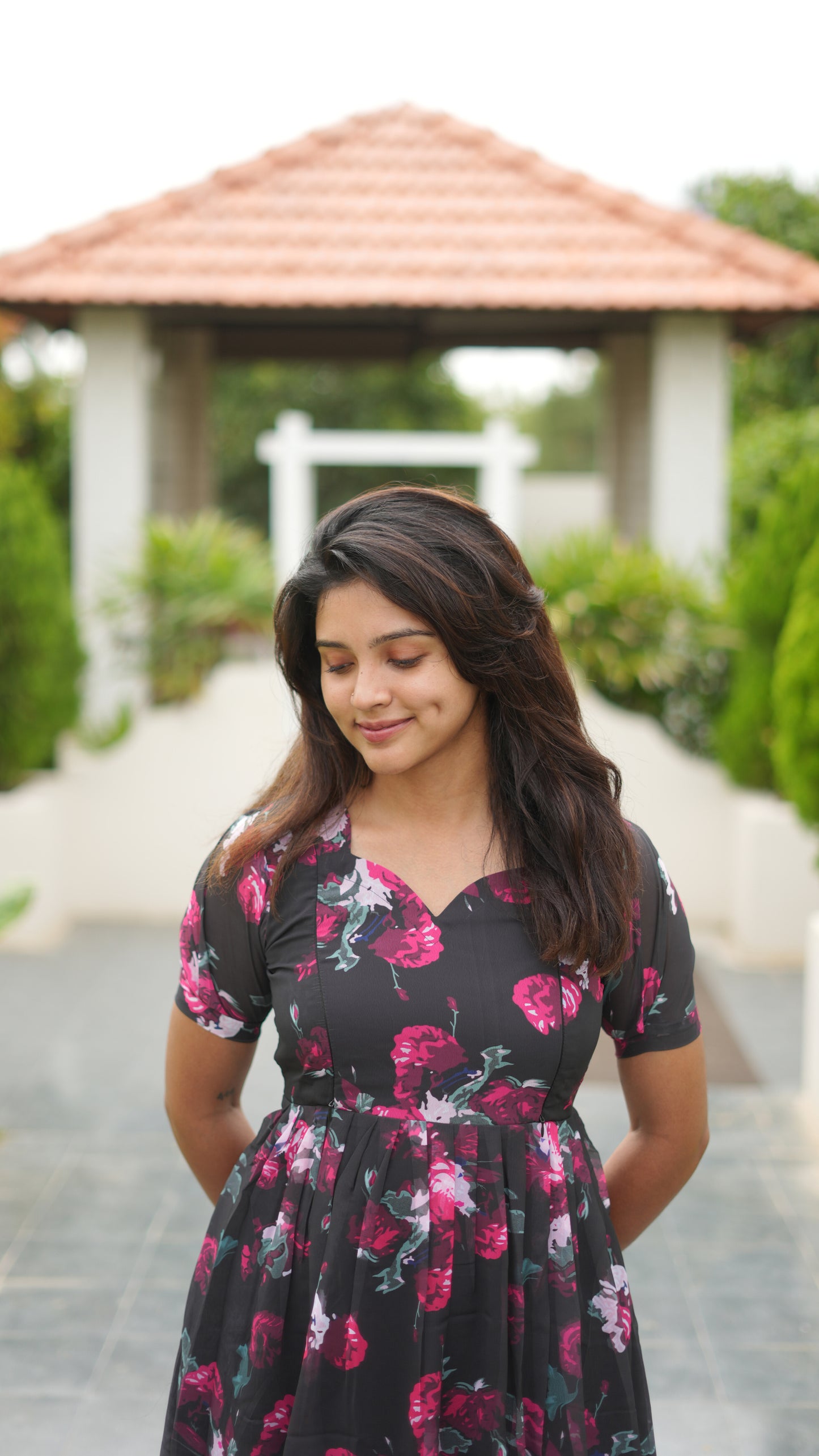 Woman wearing a floral dress standing outdoors with a gazebo in the background