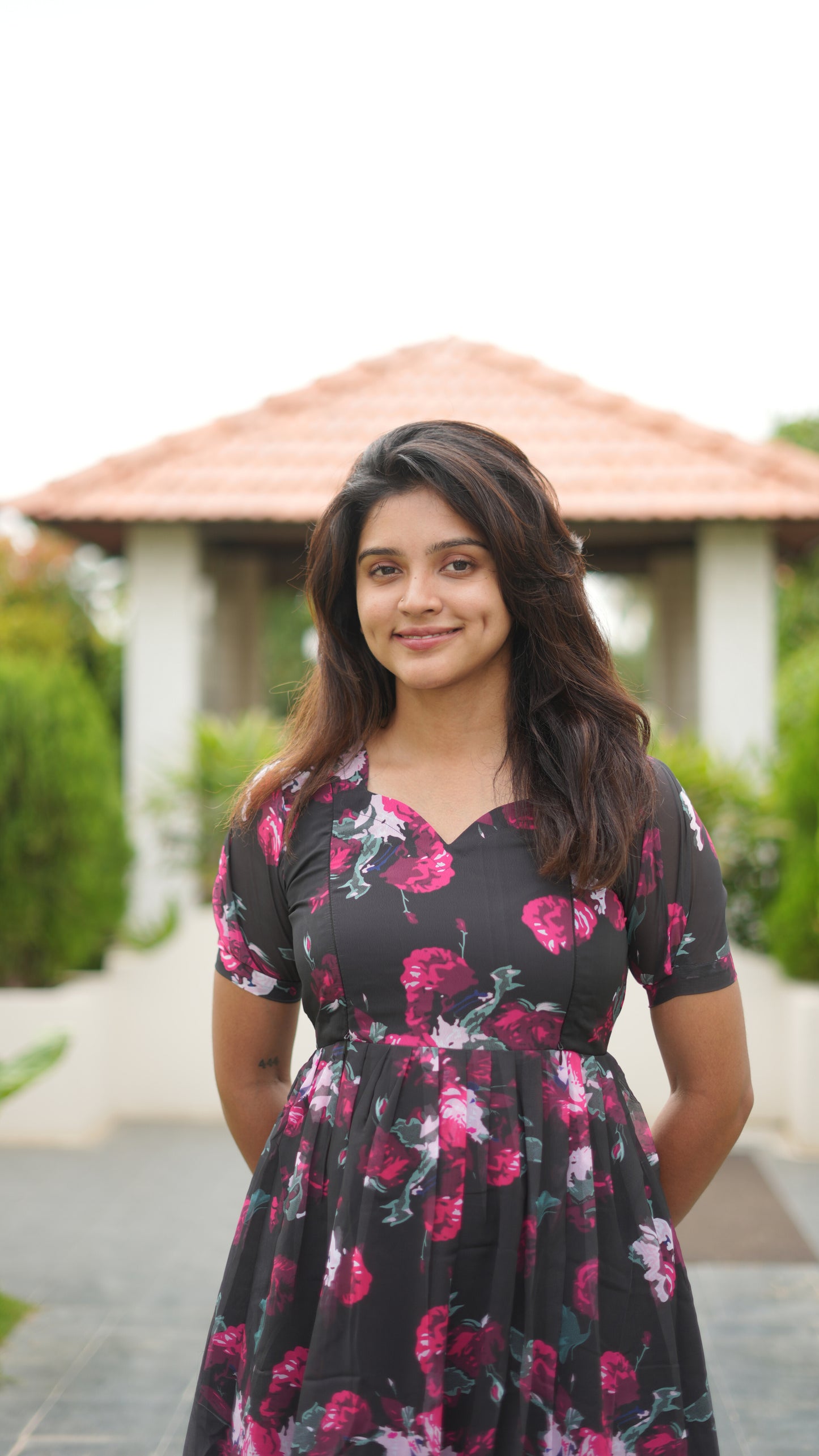 Woman wearing a black floral dress standing outdoors with a gazebo in the background