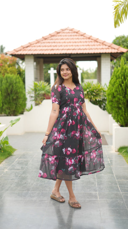 Woman wearing a black dress with pink floral patterns in an outdoor setting.