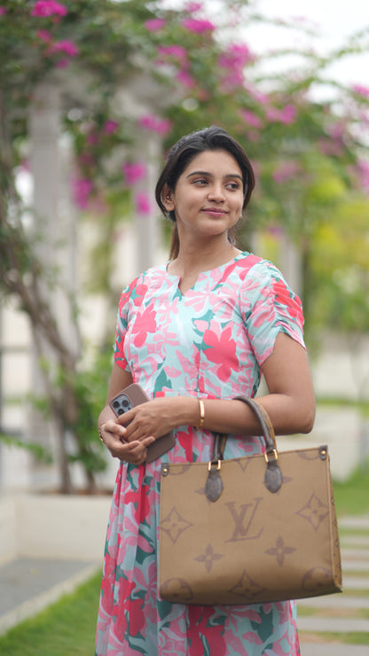 Woman holding a Louis Vuitton handbag with a floral dress in an outdoor setting