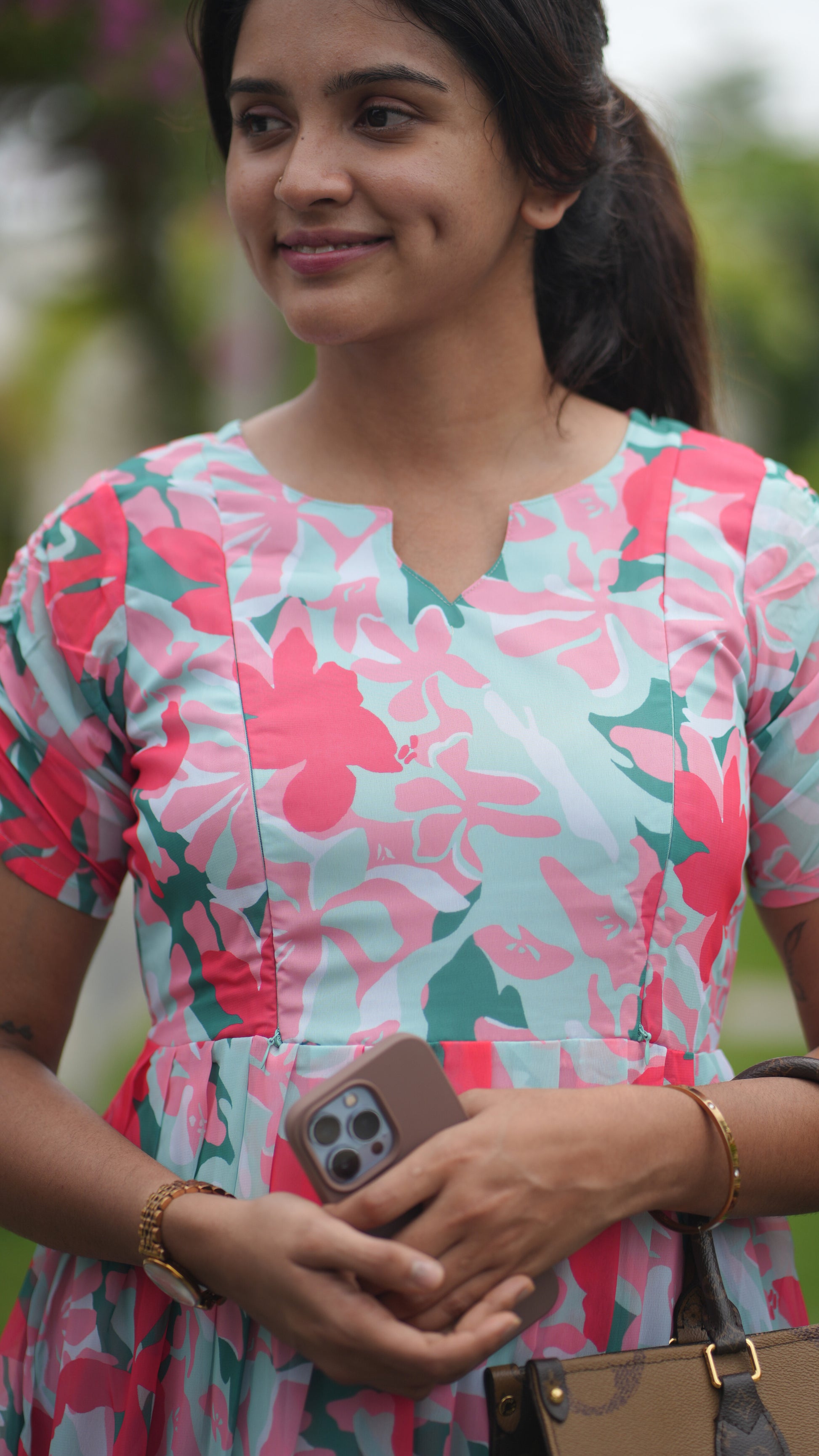 Woman wearing a pink and green floral dress holding a phone.