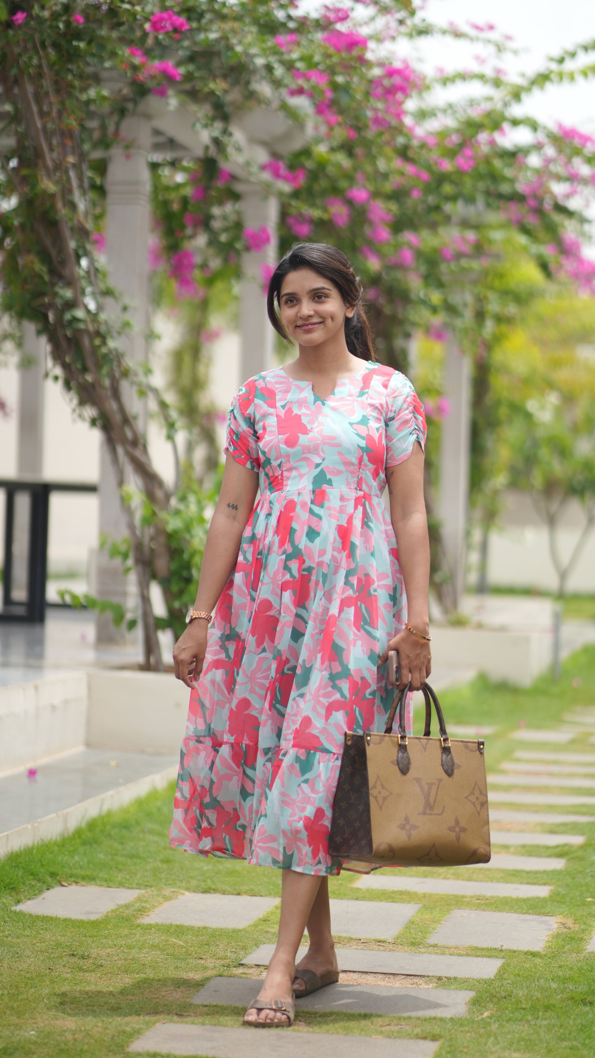 Woman in a floral dress standing outdoors with greenery and flowers in the background
