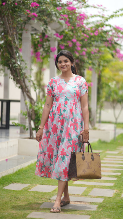 Woman in a floral dress standing outdoors with greenery and flowers in the background
