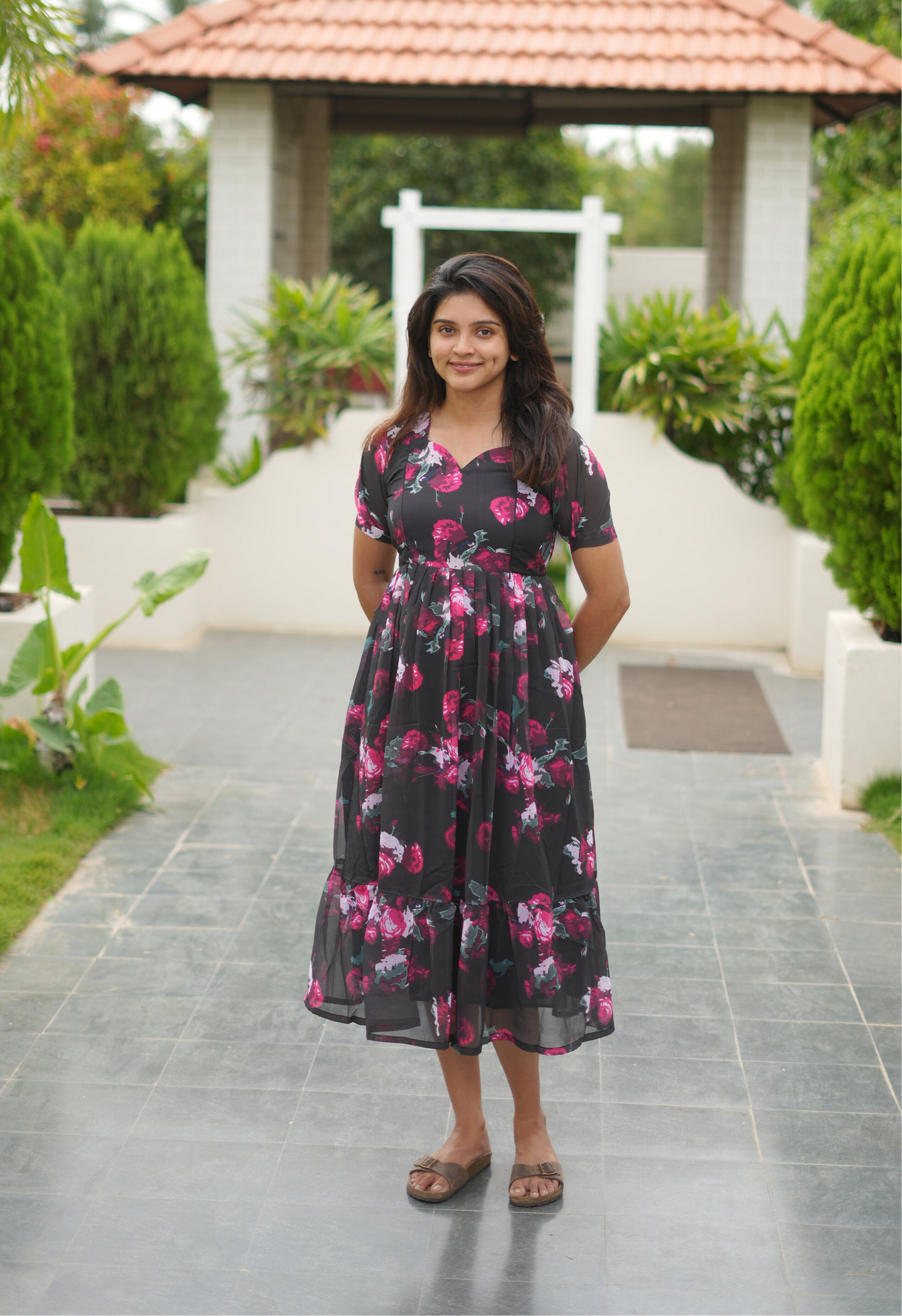 Woman in a floral dress standing on a pathway with greenery in the background