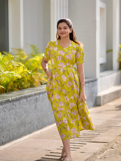 A woman standing on a pathway wearing a neon green maxi dress with a floral pattern, featuring adjustable straps and two visible zippers.